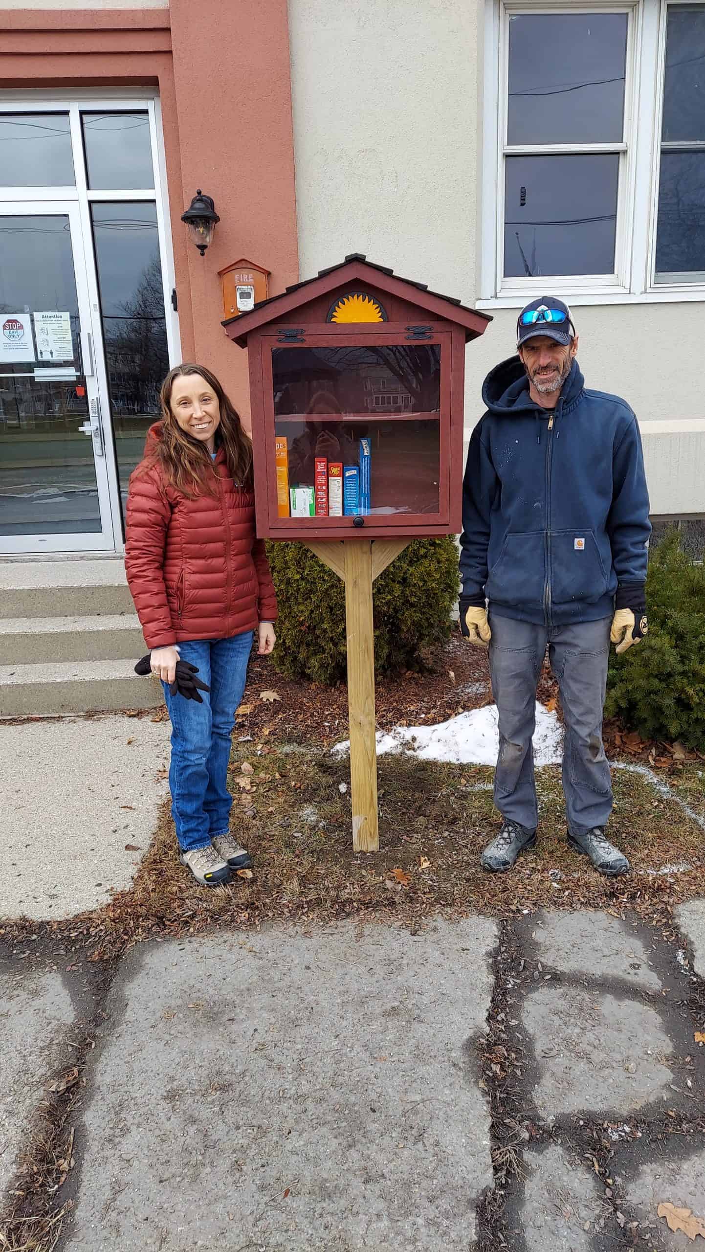 Carmen and Kenny stand beside a newly installed Little free Pantry